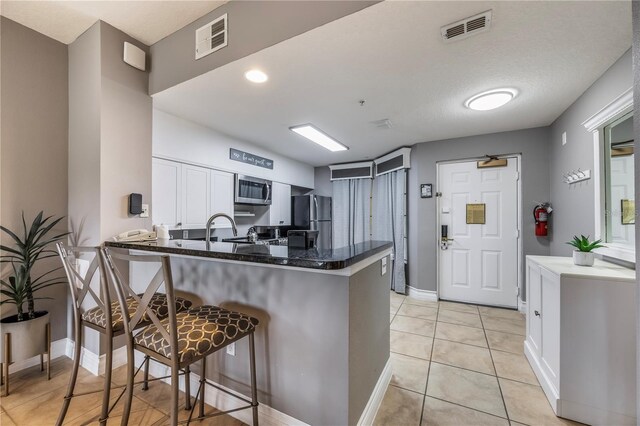 kitchen with kitchen peninsula, a breakfast bar, white cabinets, light tile patterned floors, and appliances with stainless steel finishes