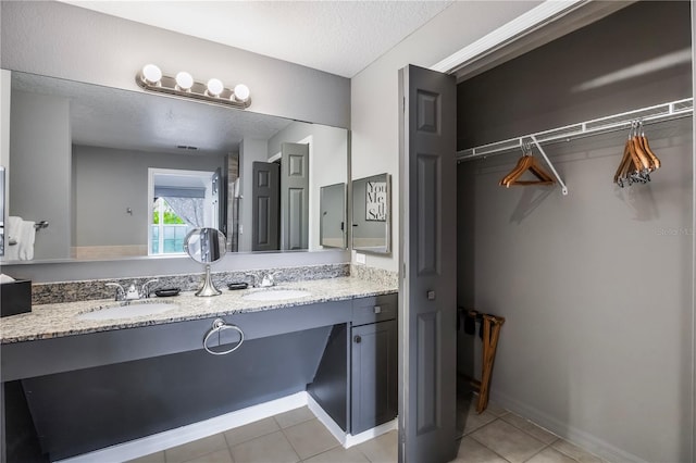 bathroom with a spacious closet, tile patterned floors, a sink, and a textured ceiling