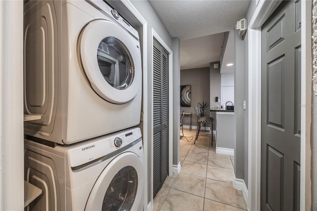 clothes washing area featuring a textured ceiling, baseboards, stacked washer / dryer, laundry area, and light tile patterned floors