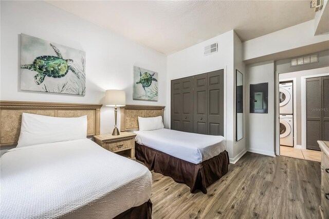 bedroom featuring stacked washer / drying machine, wood finished floors, visible vents, a closet, and baseboards