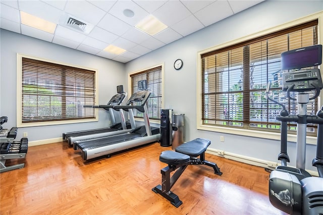 workout area featuring a paneled ceiling and light parquet flooring