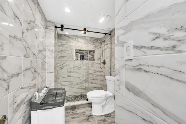 bathroom featuring a tile shower, vanity, tile walls, and toilet