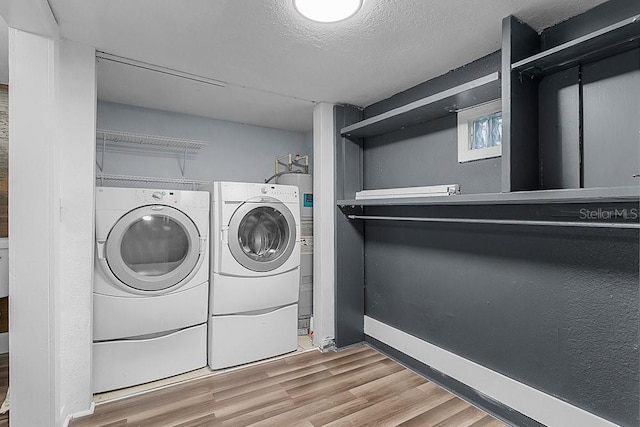 clothes washing area featuring washing machine and dryer, wood-type flooring, and a textured ceiling