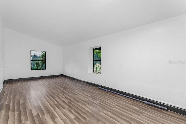 empty room featuring lofted ceiling, light wood-type flooring, and a healthy amount of sunlight