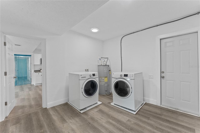 clothes washing area featuring a textured ceiling, electric water heater, washing machine and clothes dryer, and light wood-type flooring