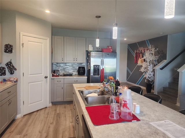 kitchen with hanging light fixtures, gray cabinetry, sink, light wood-type flooring, and appliances with stainless steel finishes