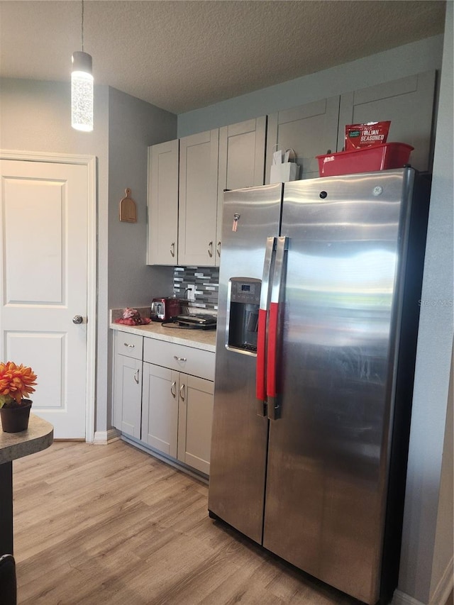 kitchen featuring stainless steel fridge, backsplash, a textured ceiling, light hardwood / wood-style flooring, and decorative light fixtures