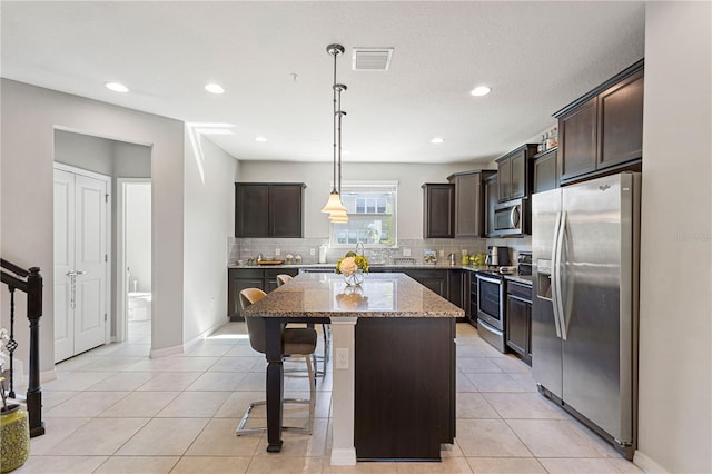 kitchen with pendant lighting, a kitchen island, dark brown cabinetry, light stone counters, and stainless steel appliances