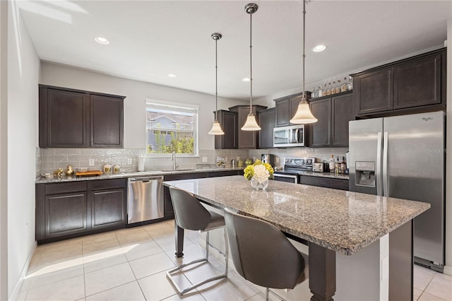 kitchen with pendant lighting, appliances with stainless steel finishes, a kitchen breakfast bar, a center island, and light stone countertops