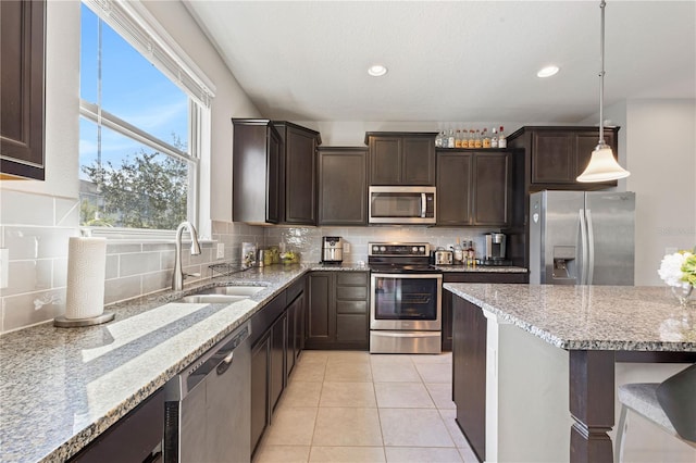 kitchen featuring light stone counters, tasteful backsplash, sink, hanging light fixtures, and appliances with stainless steel finishes