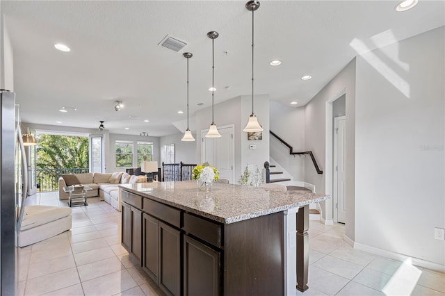 kitchen with dark brown cabinetry, a breakfast bar, light stone counters, hanging light fixtures, and light tile patterned floors