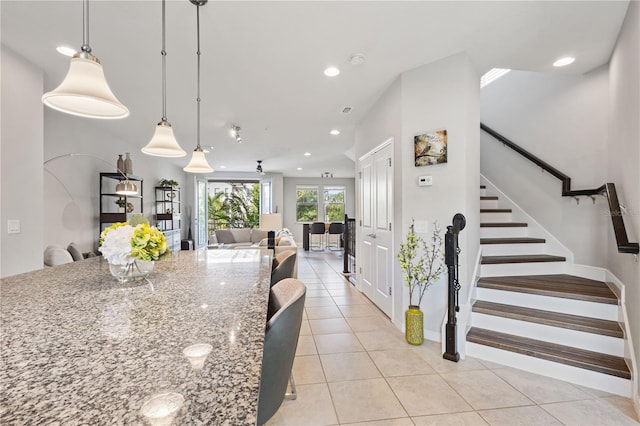 kitchen with hanging light fixtures, a breakfast bar area, light stone counters, and light tile patterned floors