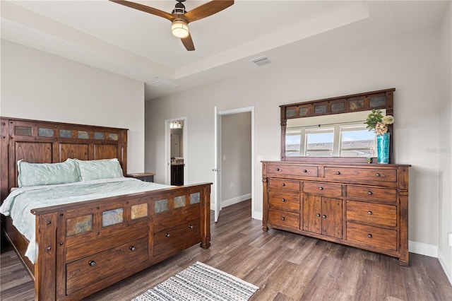 bedroom featuring ceiling fan, ensuite bath, a raised ceiling, and dark hardwood / wood-style flooring