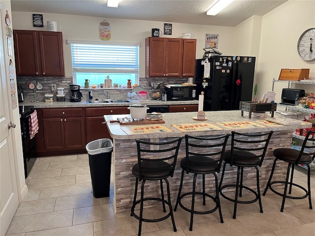 kitchen featuring backsplash, a kitchen bar, black appliances, sink, and a center island