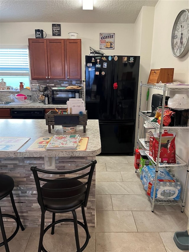 kitchen with a kitchen breakfast bar, light tile patterned flooring, a textured ceiling, and black appliances