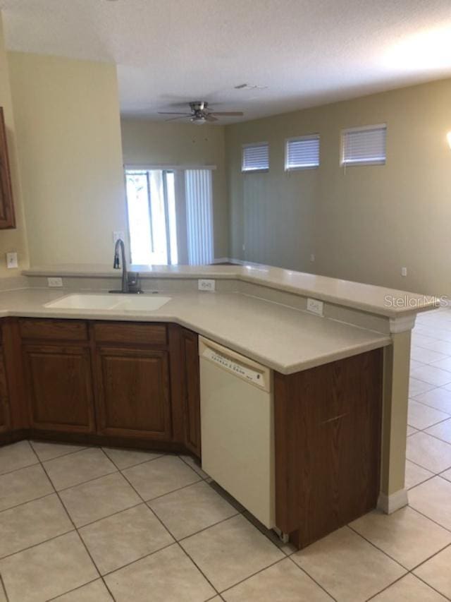 kitchen with light tile patterned flooring, kitchen peninsula, sink, and white dishwasher