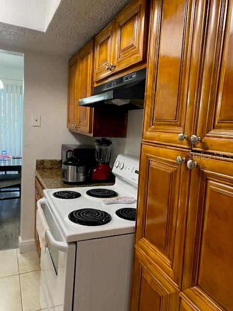 kitchen with a textured ceiling, dark stone countertops, light tile patterned floors, and electric range