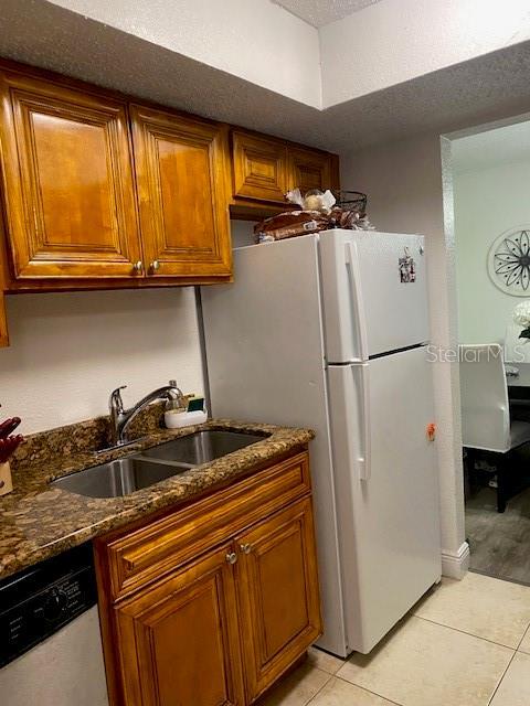 kitchen with brown cabinetry, a sink, dishwashing machine, and light tile patterned floors