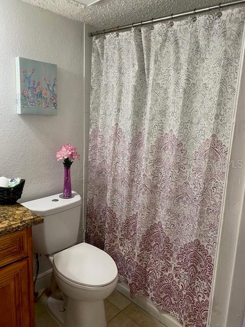 bathroom with tile patterned flooring, a textured wall, toilet, vanity, and a shower with shower curtain