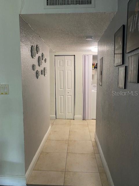 hallway featuring electric panel, a textured ceiling, baseboards, visible vents, and light tile patterned floors
