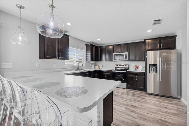 kitchen featuring light wood-type flooring, dark brown cabinets, decorative light fixtures, stainless steel appliances, and kitchen peninsula