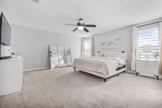 bedroom with ceiling fan, a textured ceiling, light carpet, and multiple windows