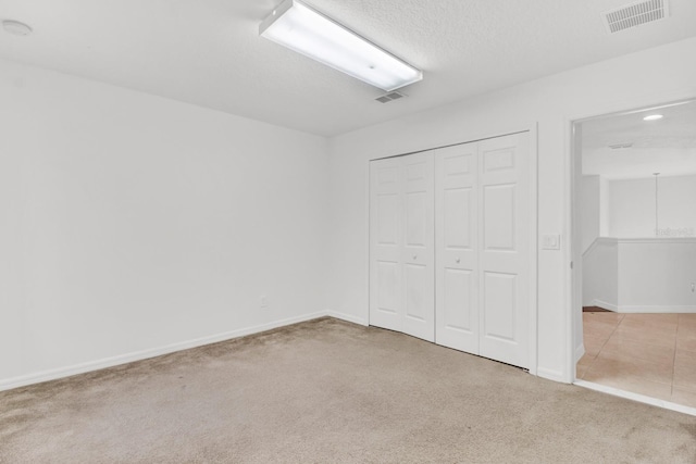 unfurnished bedroom featuring a closet, a textured ceiling, and light carpet