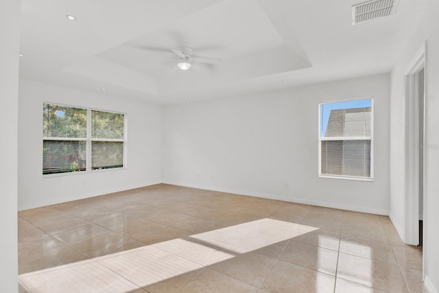 spare room featuring ceiling fan, a tray ceiling, and light tile patterned floors