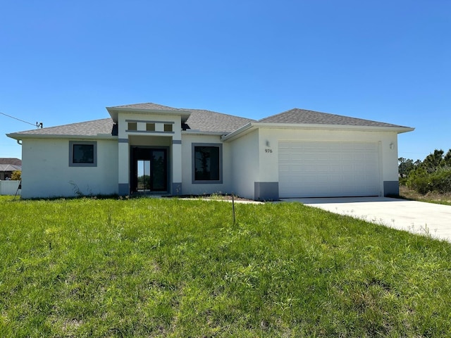 prairie-style home with stucco siding, a shingled roof, concrete driveway, an attached garage, and a front yard