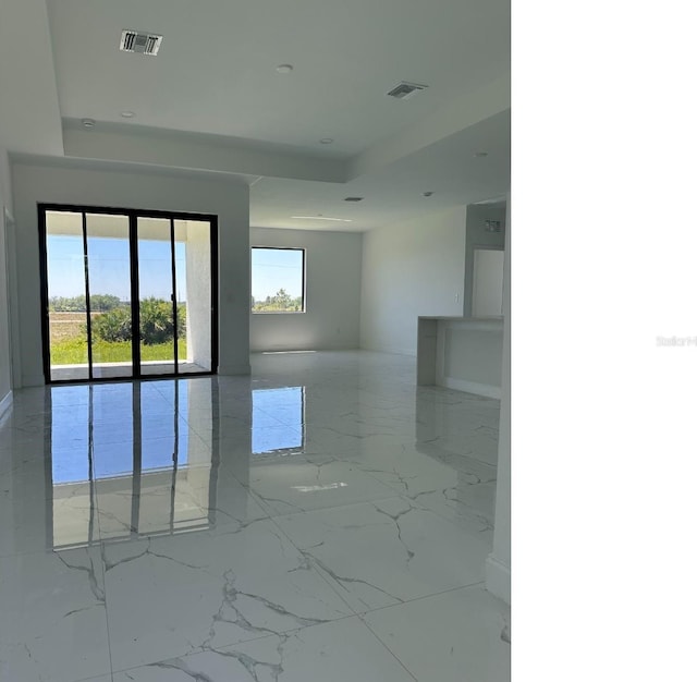 empty room with marble finish floor, visible vents, and a tray ceiling