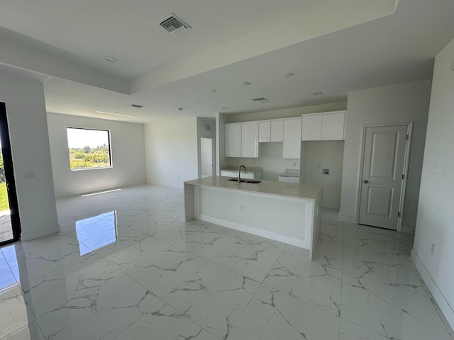 kitchen with a kitchen island with sink, sink, and white cabinets