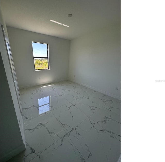 spare room featuring marble finish floor and baseboards