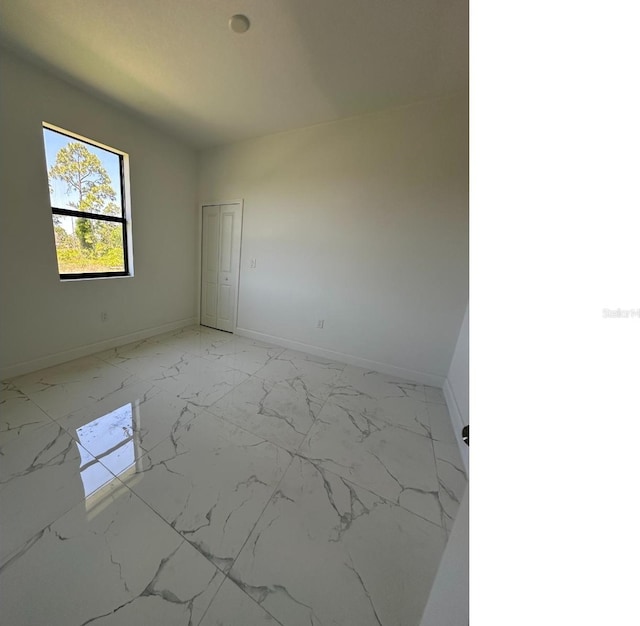 spare room featuring marble finish floor and baseboards