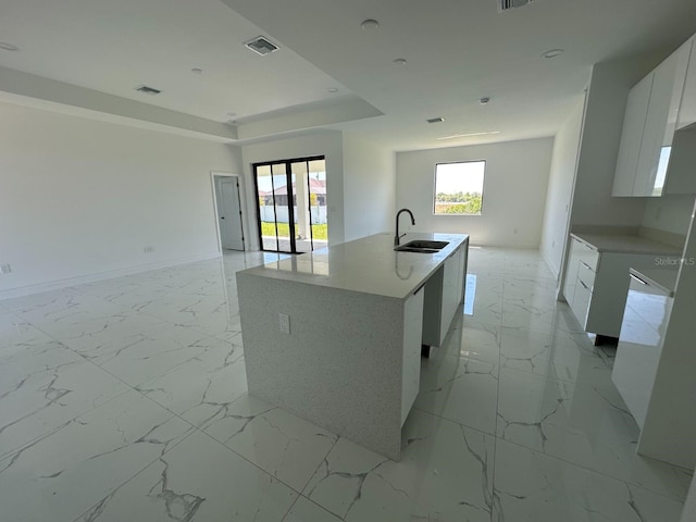 kitchen featuring an island with sink, a raised ceiling, sink, french doors, and white cabinetry