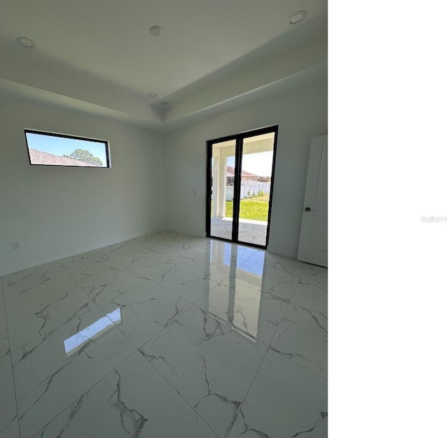 unfurnished room with marble finish floor, a tray ceiling, and baseboards