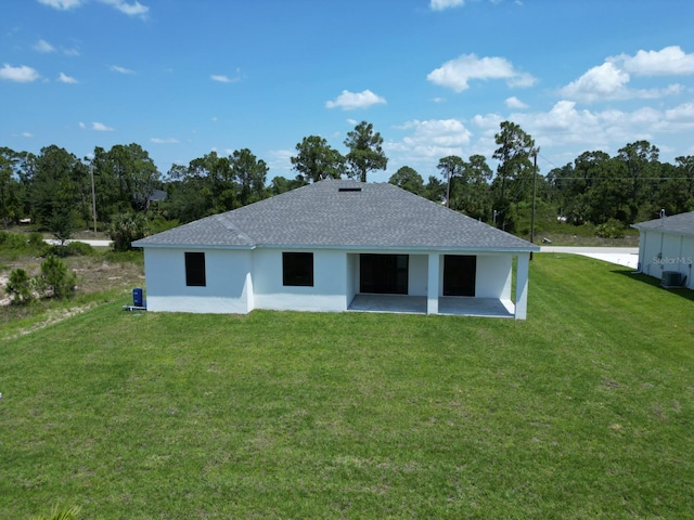 back of property with a yard, a shingled roof, stucco siding, and a patio