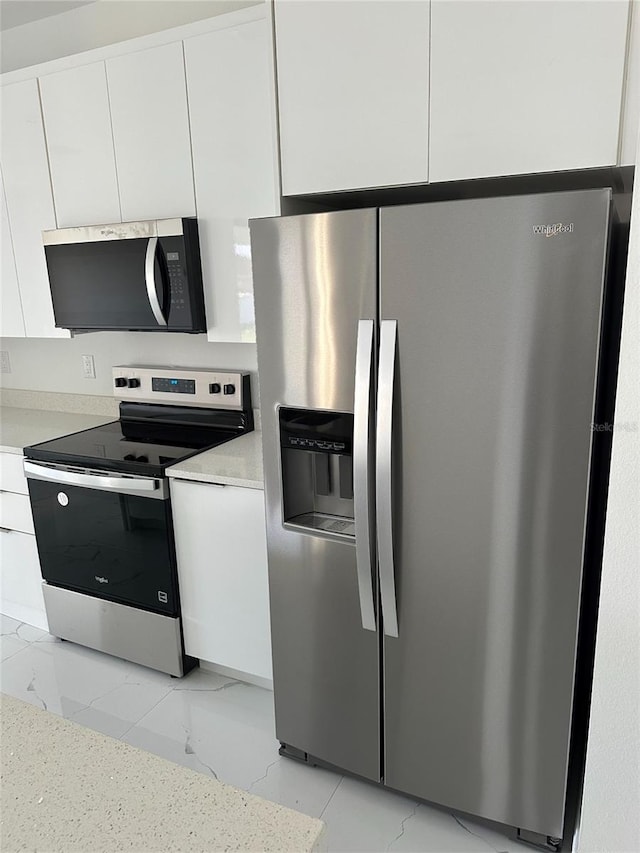 kitchen with marble finish floor, appliances with stainless steel finishes, white cabinets, and light countertops