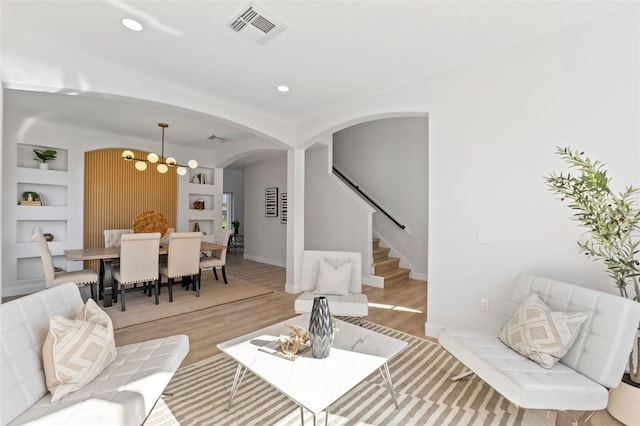 living room featuring built in features, light hardwood / wood-style flooring, and an inviting chandelier