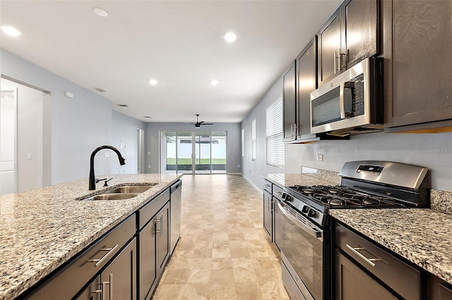 kitchen with ceiling fan, dark brown cabinetry, sink, stainless steel appliances, and light stone countertops