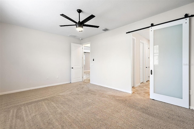 unfurnished room featuring light carpet, ceiling fan, and a barn door