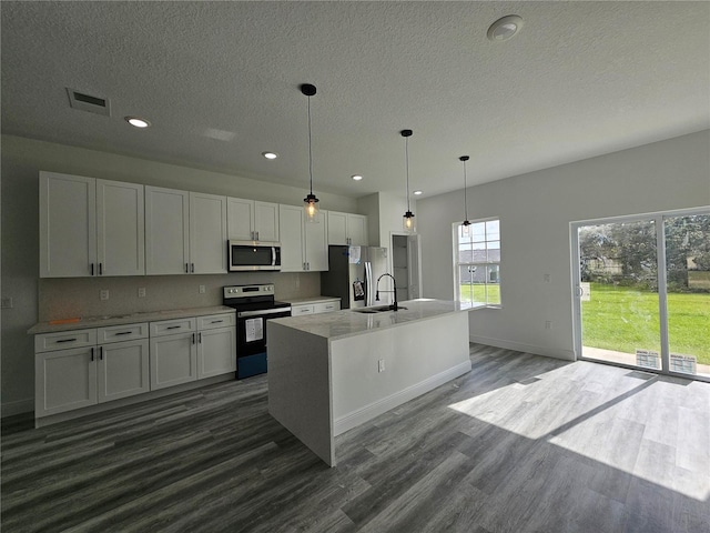 kitchen with white cabinets, stainless steel appliances, a center island with sink, and decorative light fixtures