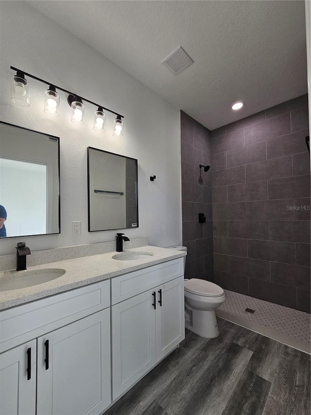 bathroom featuring vanity, hardwood / wood-style floors, a tile shower, and toilet