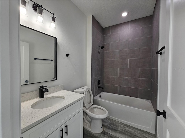 full bathroom featuring toilet, hardwood / wood-style floors, tiled shower / bath combo, vanity, and a textured ceiling