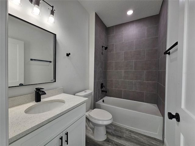 full bathroom featuring tiled shower / bath, a textured ceiling, hardwood / wood-style flooring, toilet, and vanity