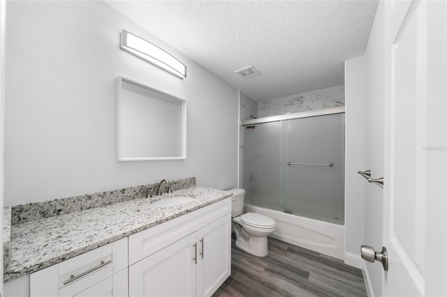 full bathroom with toilet, wood-type flooring, vanity, a textured ceiling, and shower / bath combination with glass door