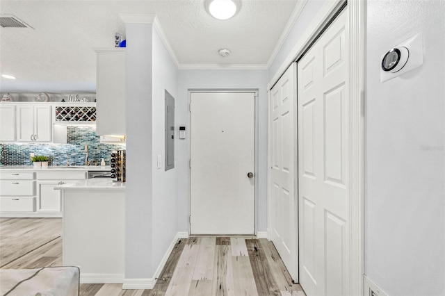 doorway with crown molding, electric panel, a textured ceiling, and light hardwood / wood-style floors