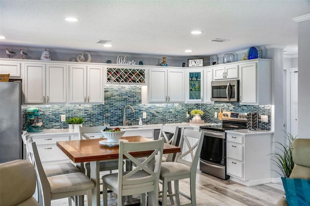 kitchen with a textured ceiling, white cabinetry, ornamental molding, light hardwood / wood-style floors, and stainless steel appliances