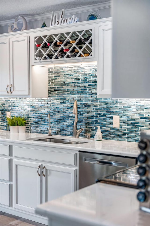 interior space featuring white cabinetry, ornamental molding, stainless steel dishwasher, and sink