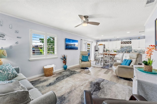 living room with sink, a textured ceiling, ceiling fan, crown molding, and light hardwood / wood-style flooring