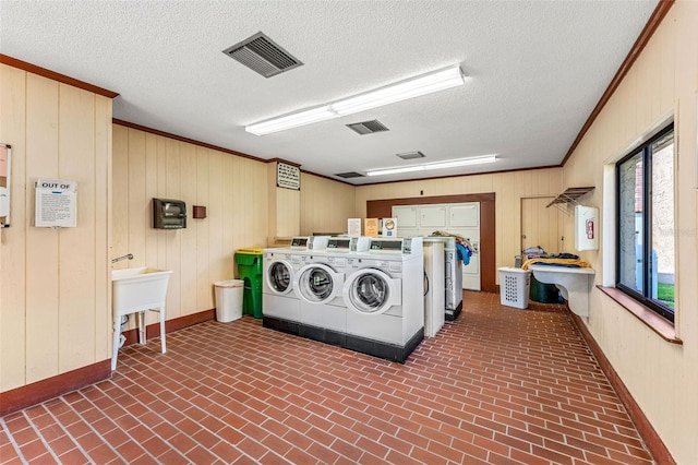 laundry room featuring wooden walls, crown molding, washing machine and dryer, and a textured ceiling